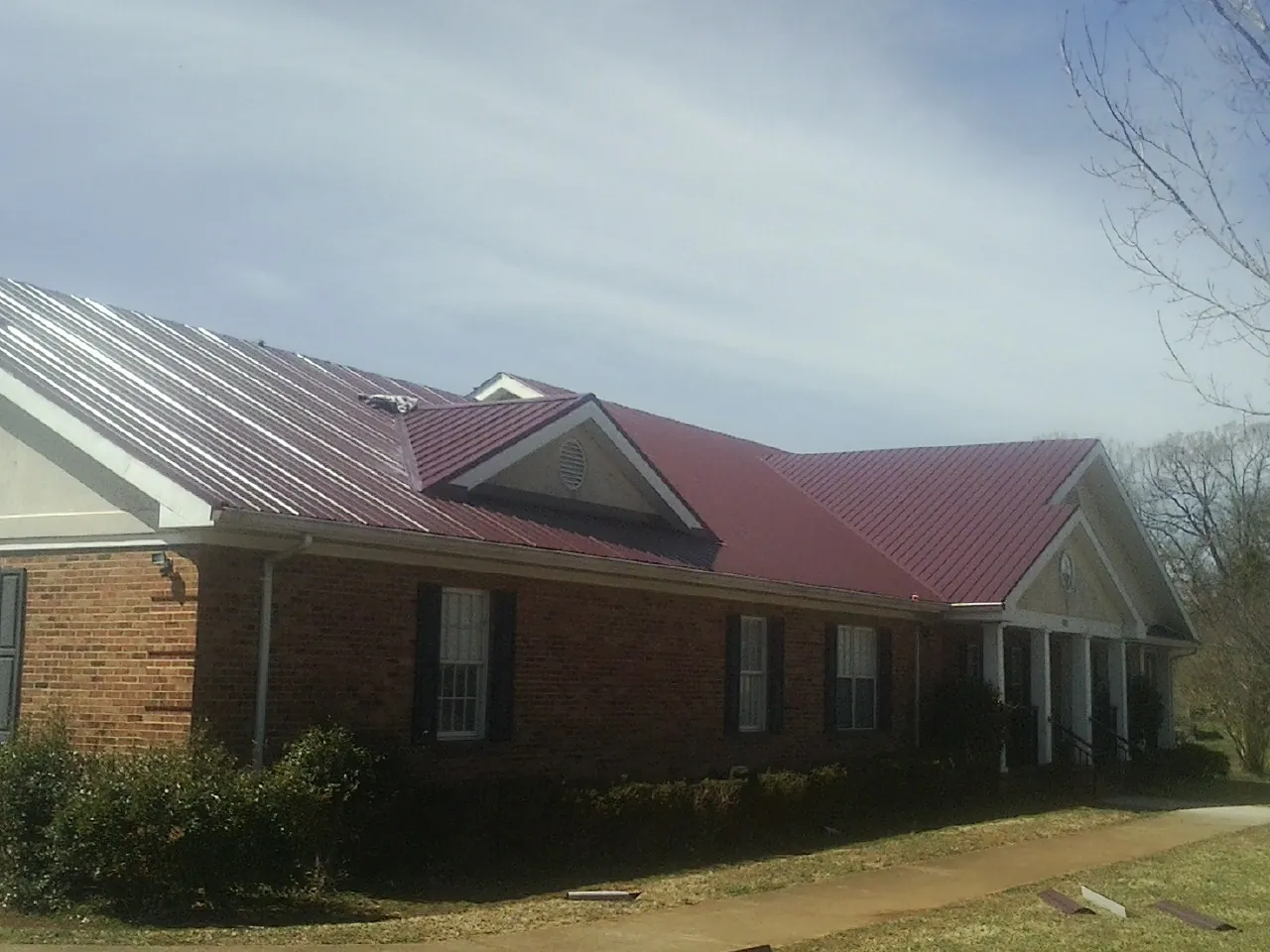 Red metal roof with gabled entries on a long brick building, from a Hail Damage Roof Repair job in Lincoln Park