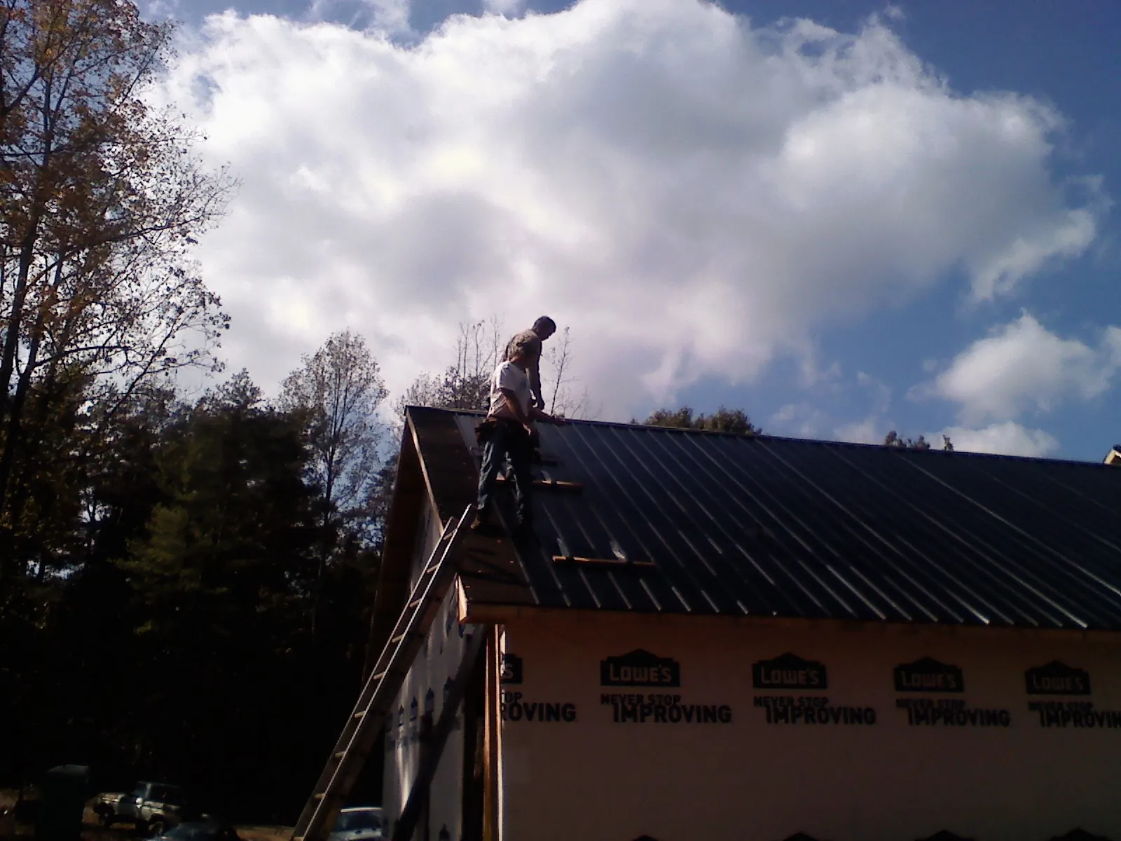 Roofer fastening dark metal panels high against a cloudy sky, from a Roof Inspection job in Lincoln Park
