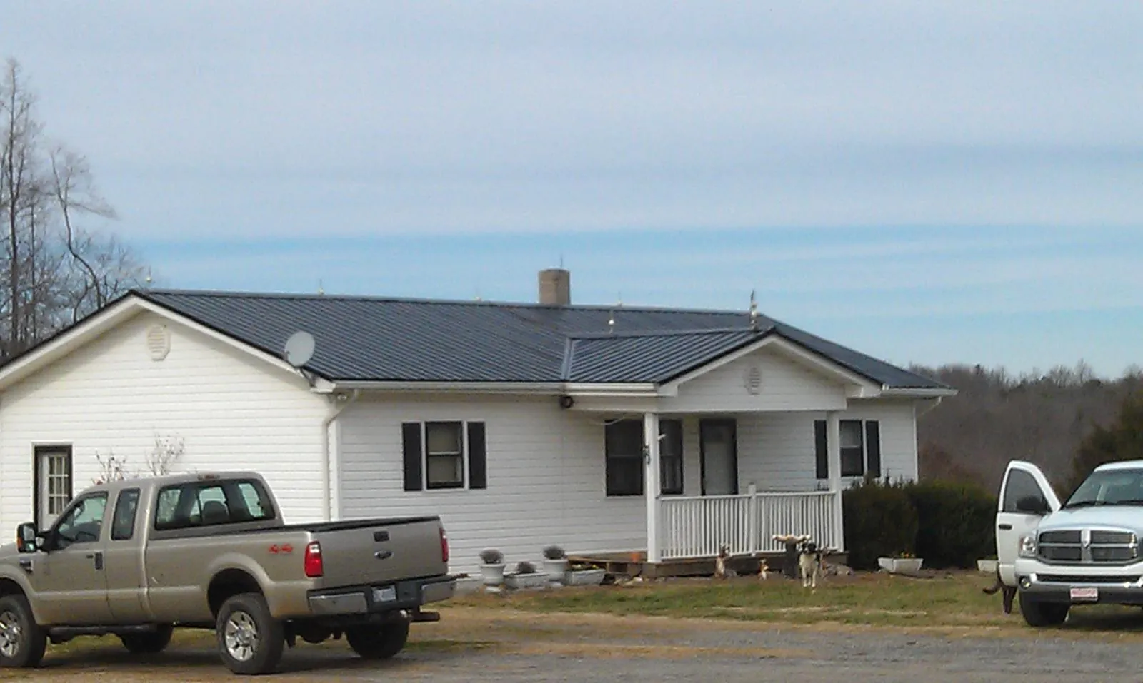 Finished dark metal roof on a white ranch home with work trucks parked in Lincoln Park
