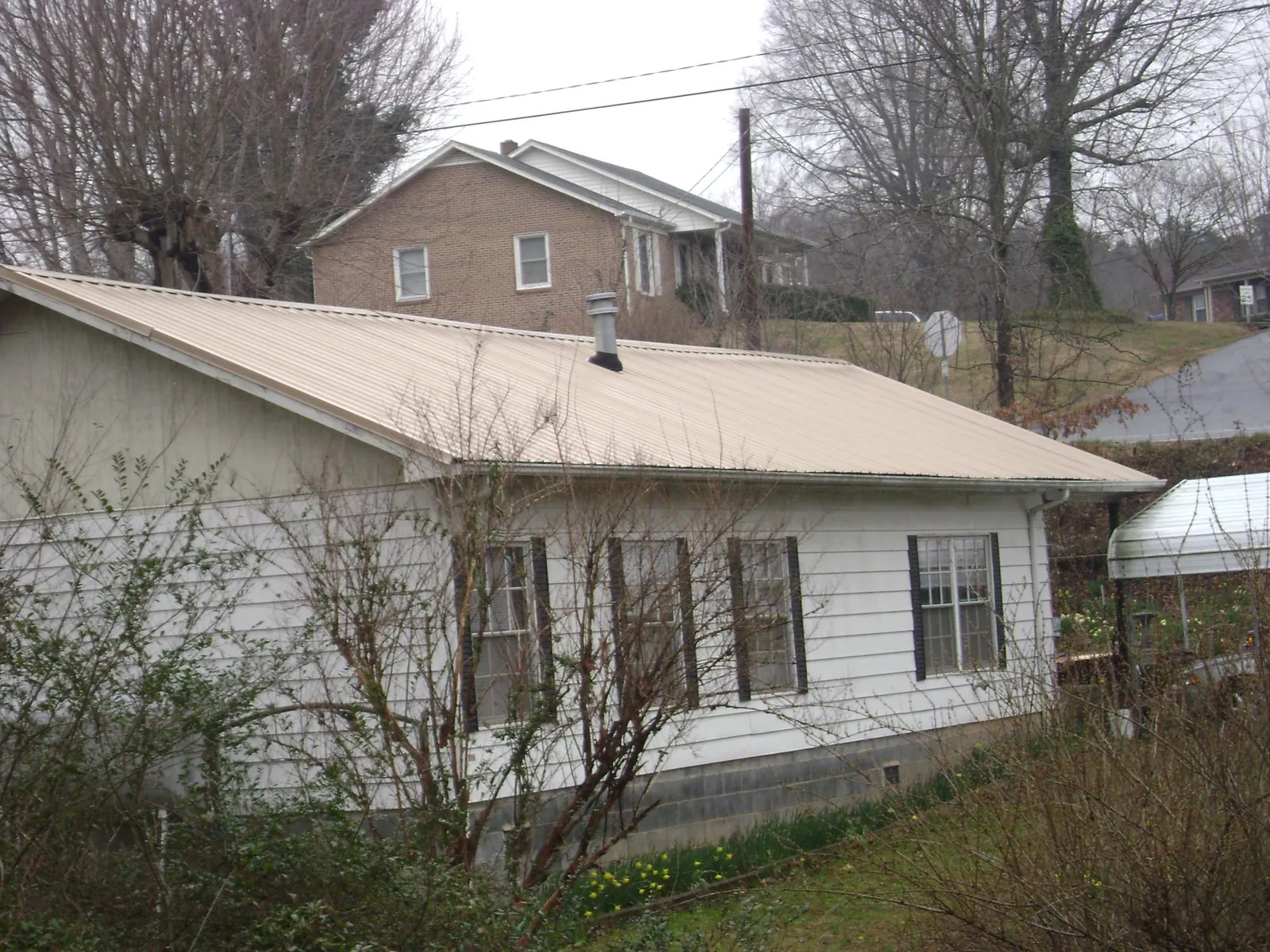 Tan metal roof on a white sided house set into a hillside — Commercial Roofing by Roofing Brothers in Lincoln Park